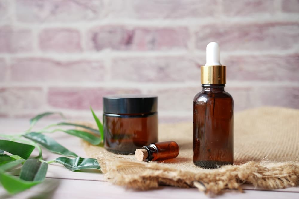 Amber glass dropper bottles of essential oil beside green leaves